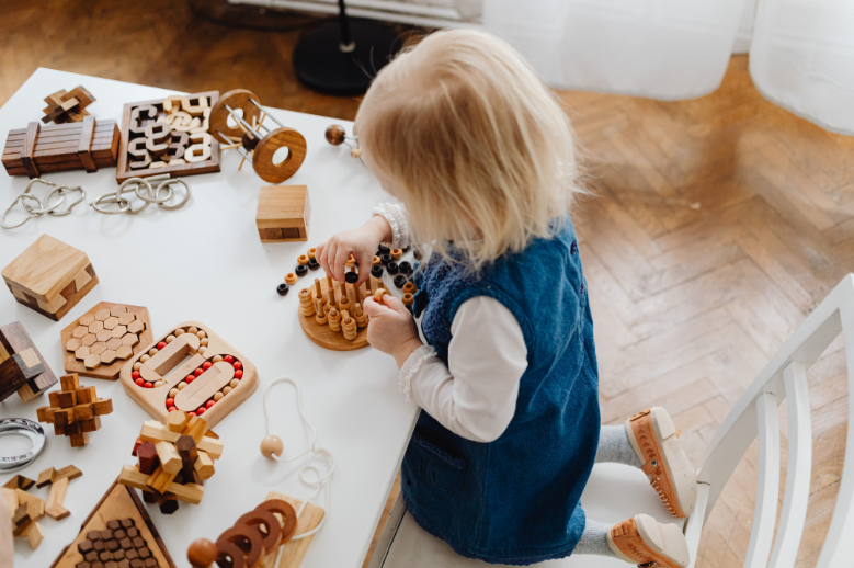 Kleines Mädchen sitzt auf dem Stuhl und spielt mit Holzspielzeug